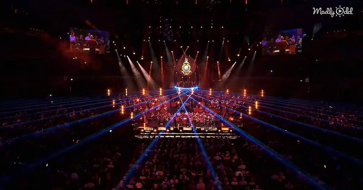 A large stage with performers, vibrant lighting, and a crowd in a dimly lit arena.