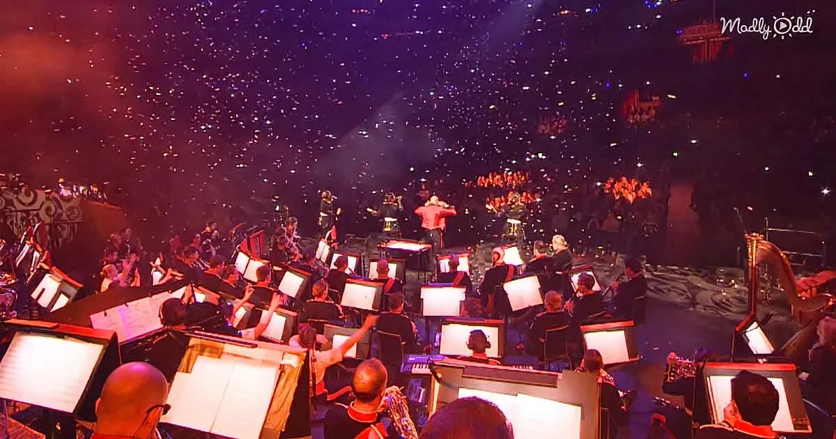 An orchestra with sheet music stands and musicians performing on stage in front of a large audience.