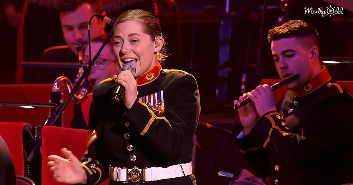 A woman in military uniform sings into a microphone while holding a red folder, with a man playing a flute in the background.