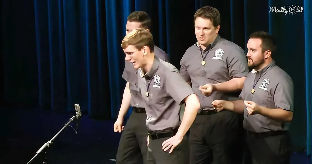 Four men in matching uniforms perform a synchronized dance on stage.