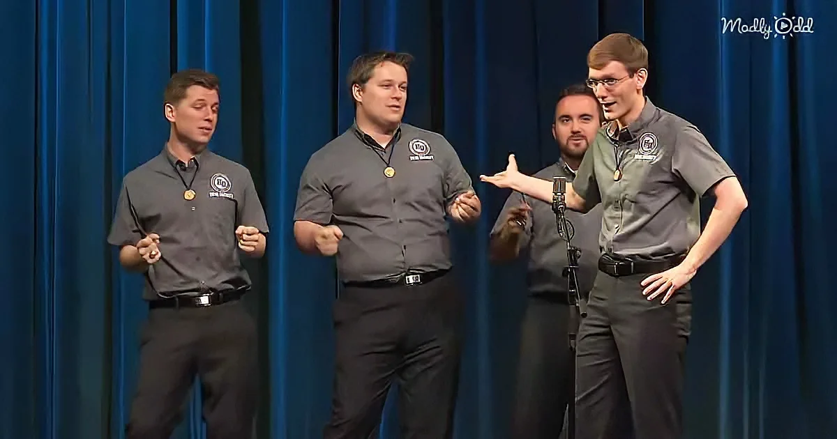 Four men in matching uniforms perform on stage with blue curtains behind them.