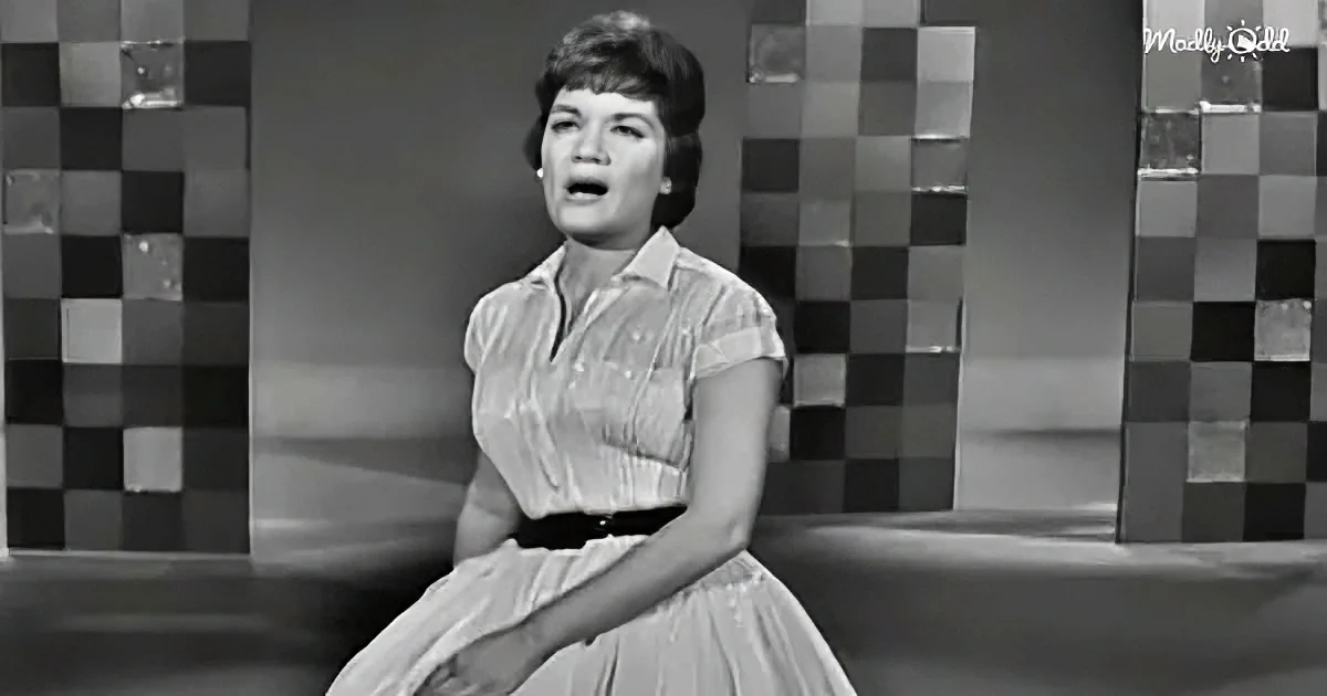 A woman in a 1950s dress sits on a stool, singing with a checkered background.
