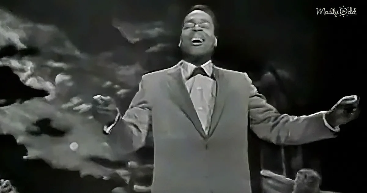 A man in a suit sings passionately with arms outstretched, set against a dark, textured background.
