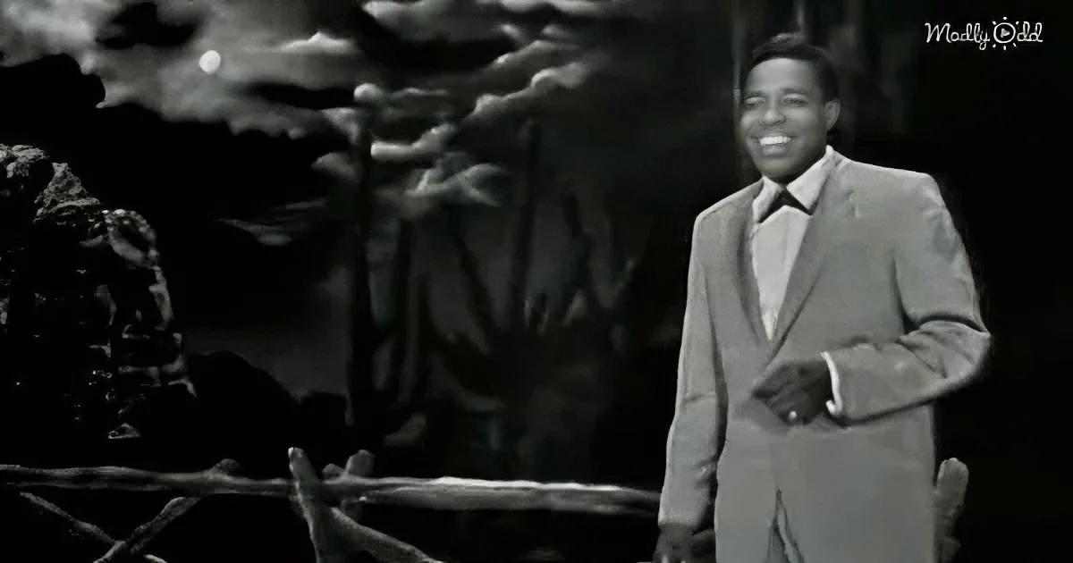 A man in a suit smiles, standing against a dark, cloudy background.