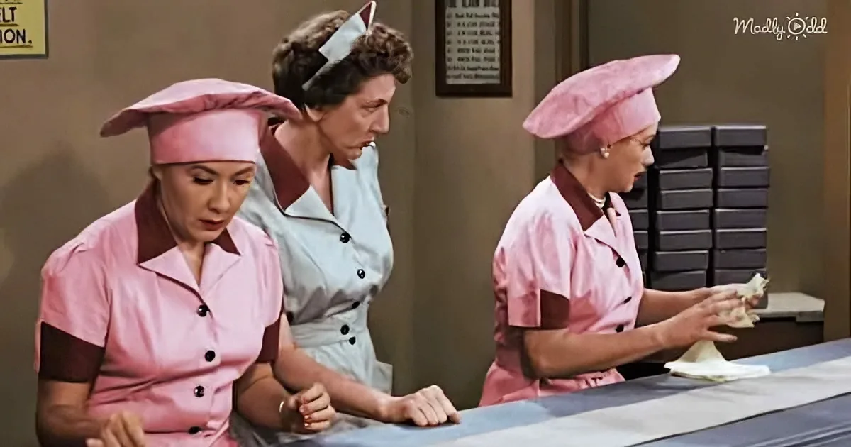 Three women in pink uniforms and hats are working at a counter, one cleaning a surface.