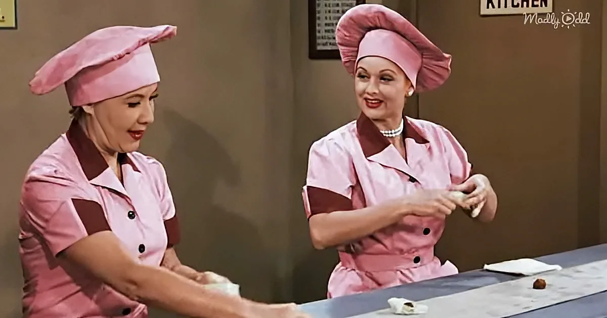 Two women in pink chef uniforms prepare food at a table in a kitchen setting.