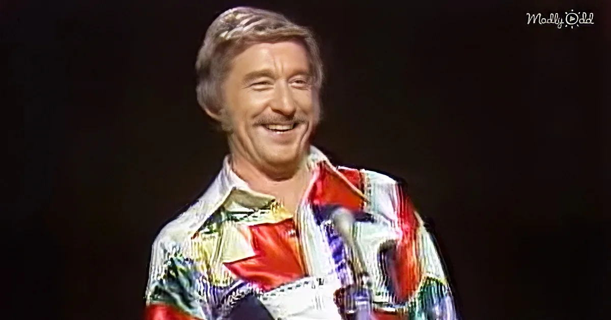 A smiling man in a colorful, patterned shirt with a red star stands against a dark background.