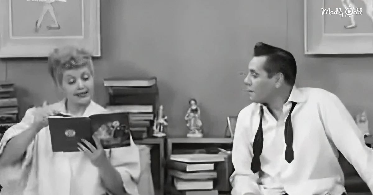 A woman in a white dress holds a book, while a man in a white shirt and tie sits beside her, both in a room with books...