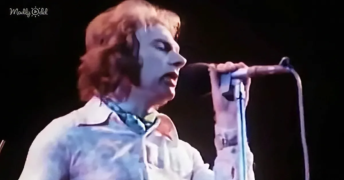 A person with long hair and a white shirt is singing into a microphone on stage.