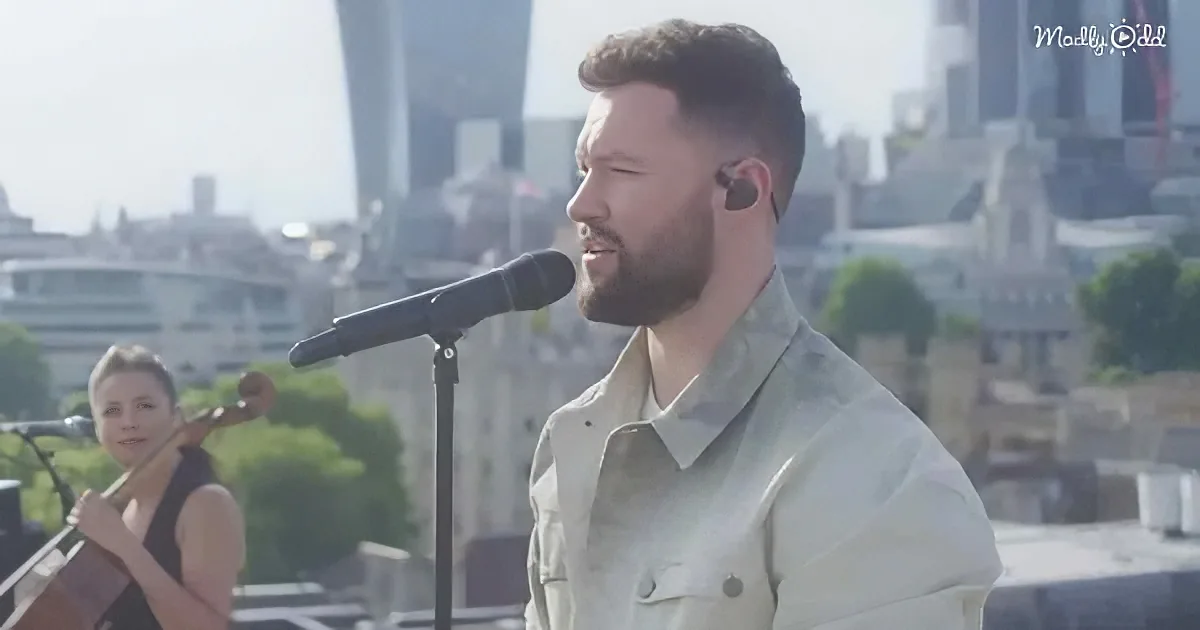 A man sings into a microphone on a rooftop with a cityscape in the background.