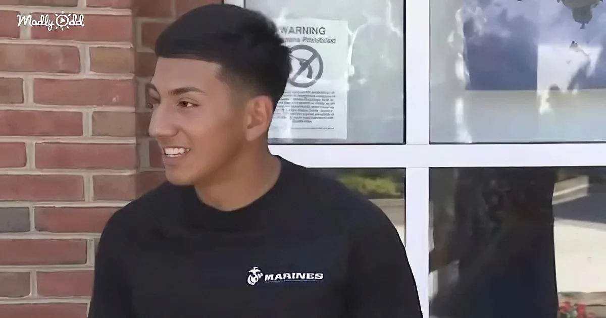 A smiling person in a black Marines shirt stands near a brick wall and a window with a "No Smoking" sign.