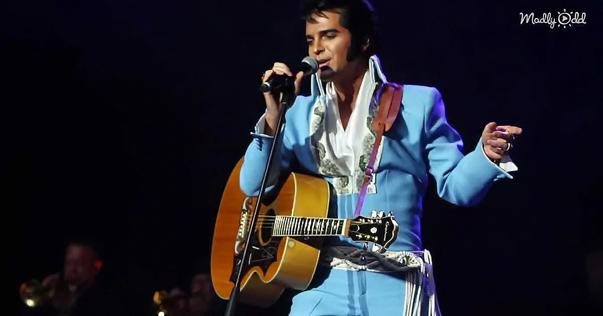 A performer in a blue suit sings into a microphone while holding an acoustic guitar on stage.