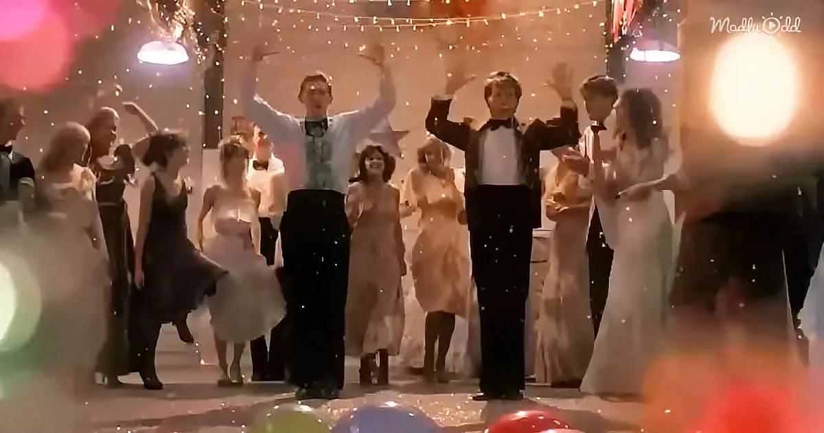 A group of people in formal attire dances joyfully under string lights, creating a festive atmosphere.