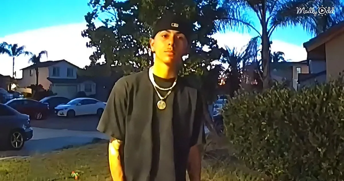 A person wearing a black shirt and cap stands outdoors in a residential area with palm trees and parked cars in the...