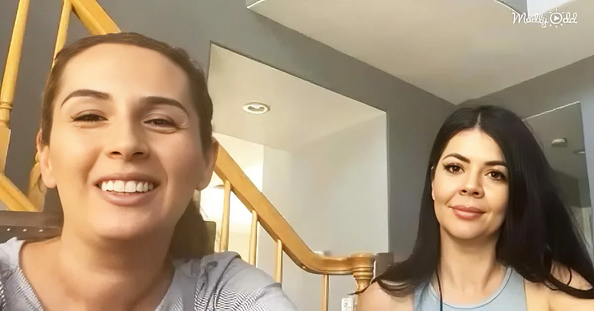 Two women smile in a selfie, one with short hair, the other with long black hair, in a home setting.