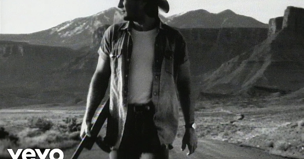 A man in a cowboy hat and shirt walks through a rugged landscape, holding a rifle.