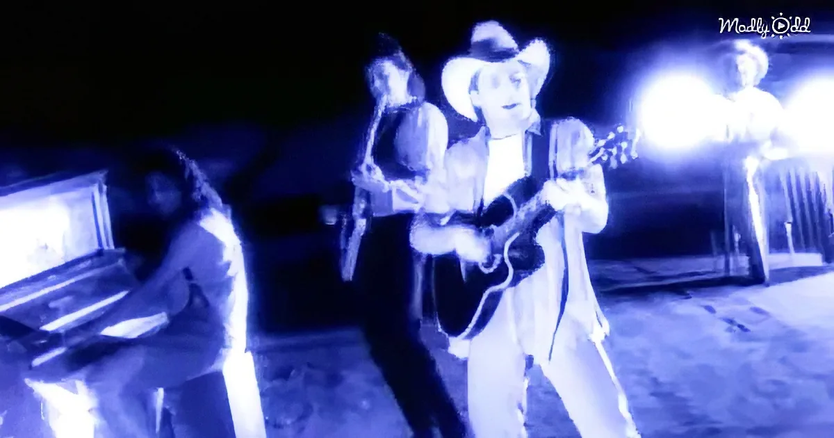 A person in a cowboy hat plays guitar under blue light, with others in the background.