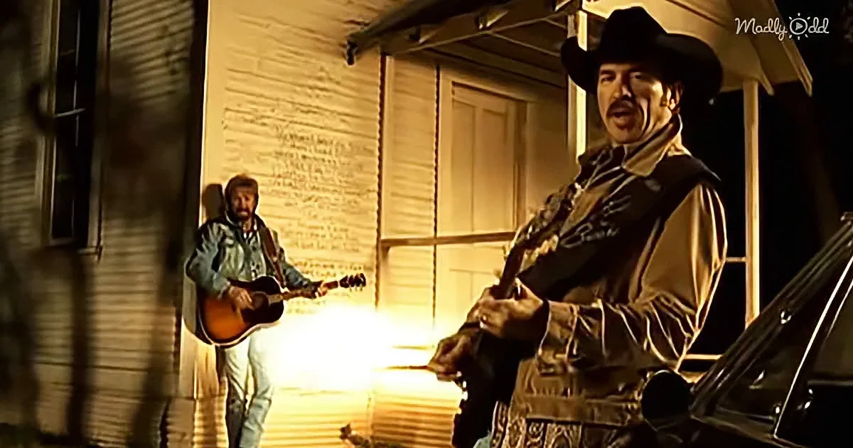A man in a cowboy hat plays guitar outside a house, illuminated by a warm light.
