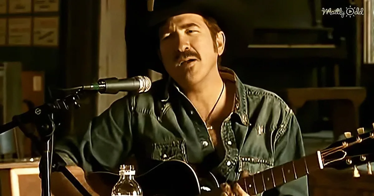 A man in a cowboy hat plays guitar and sings into a microphone in a dimly lit room.