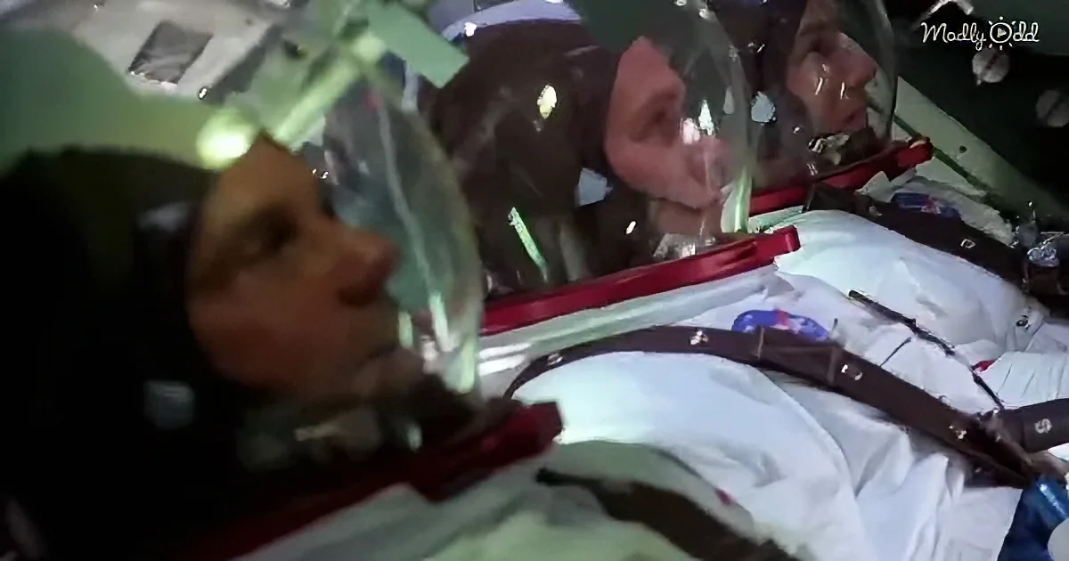 Two astronauts in space suits are floating inside a spacecraft, wearing helmets and oxygen masks.