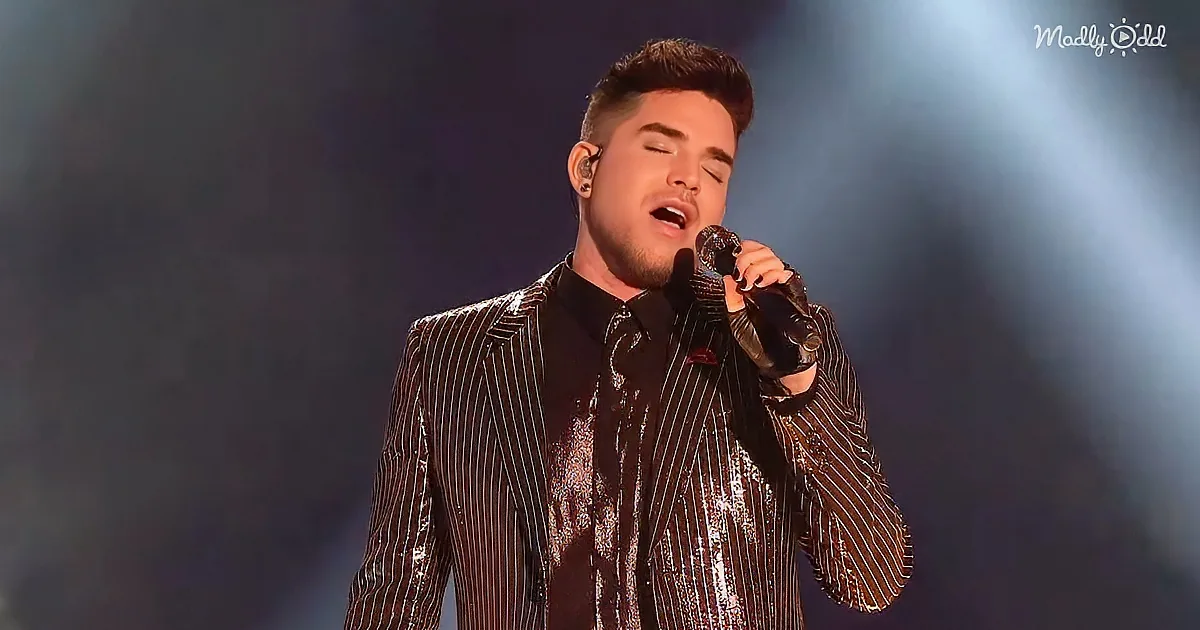 A man in a shiny, striped suit sings passionately into a microphone on stage.