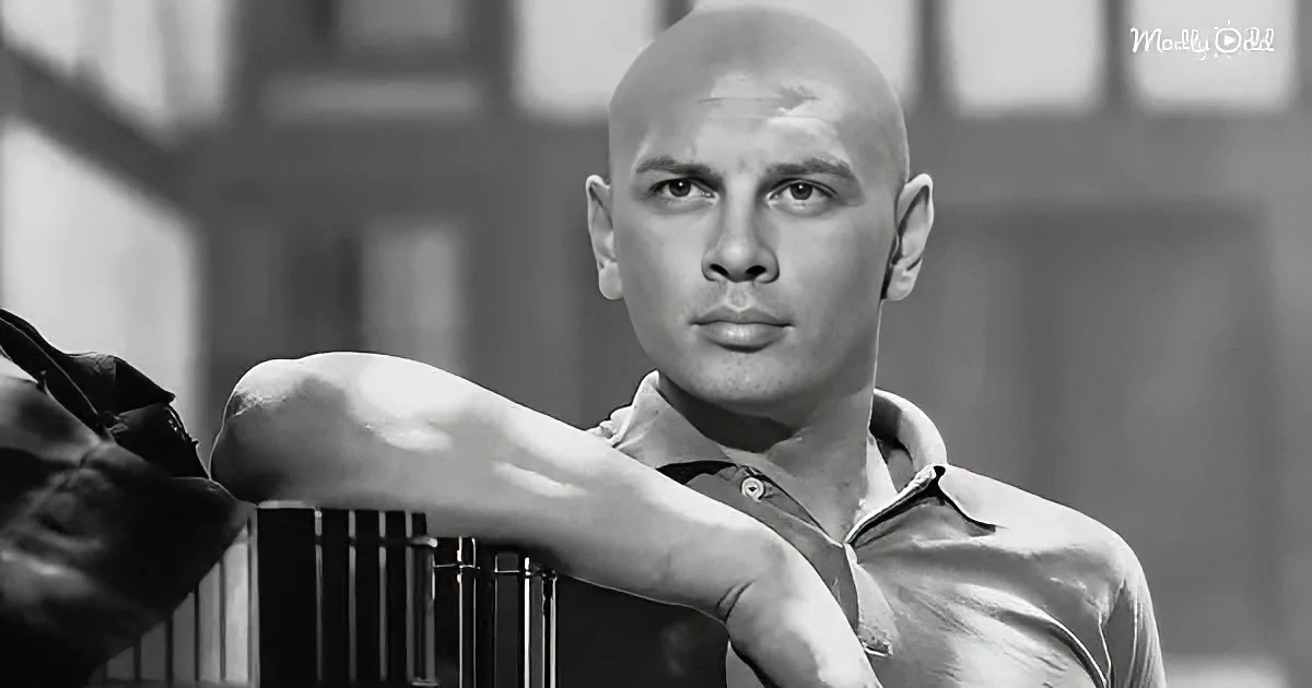 A bald man in a collared shirt leans on a railing, looking serious in a grayscale image.