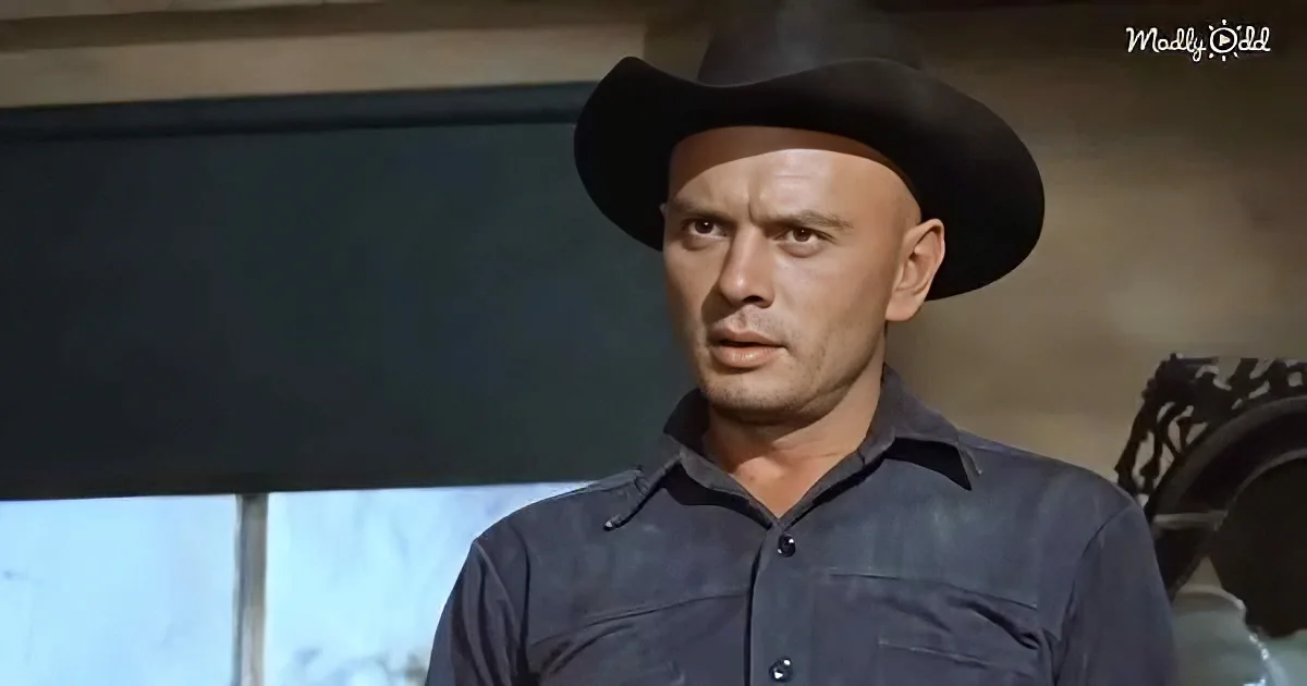 A man in a cowboy hat and dark shirt stands indoors, looking to the side with a serious expression.