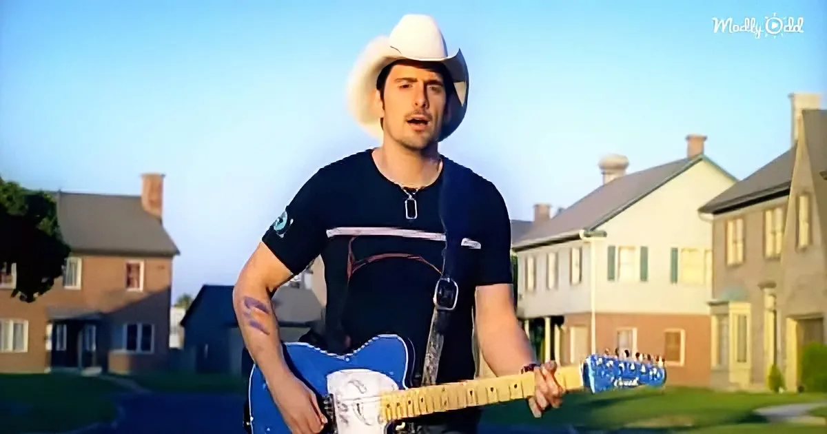 A man in a white cowboy hat plays a blue electric guitar in a suburban neighborhood.
