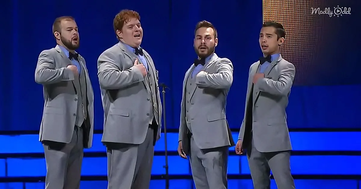 Four men in matching gray suits sing on stage with their hands on their chests.