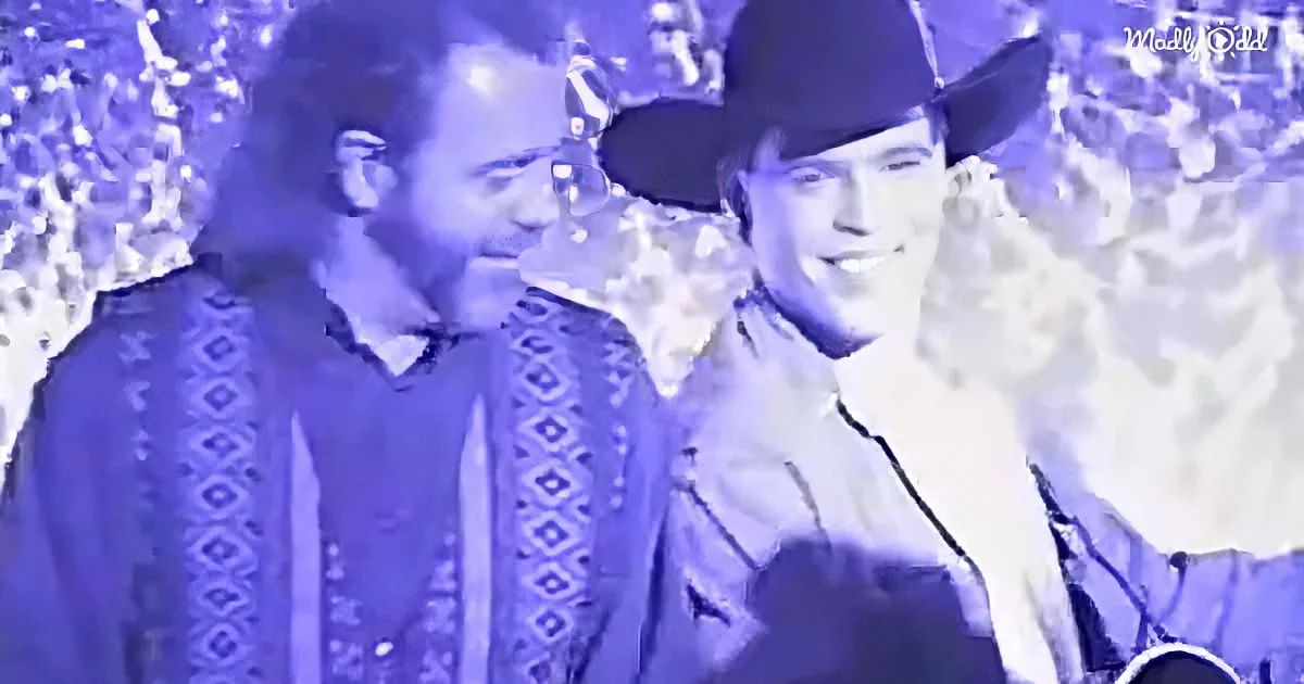 Two individuals wearing cowboy hats and patterned shirts stand side by side against a snowy backdrop.