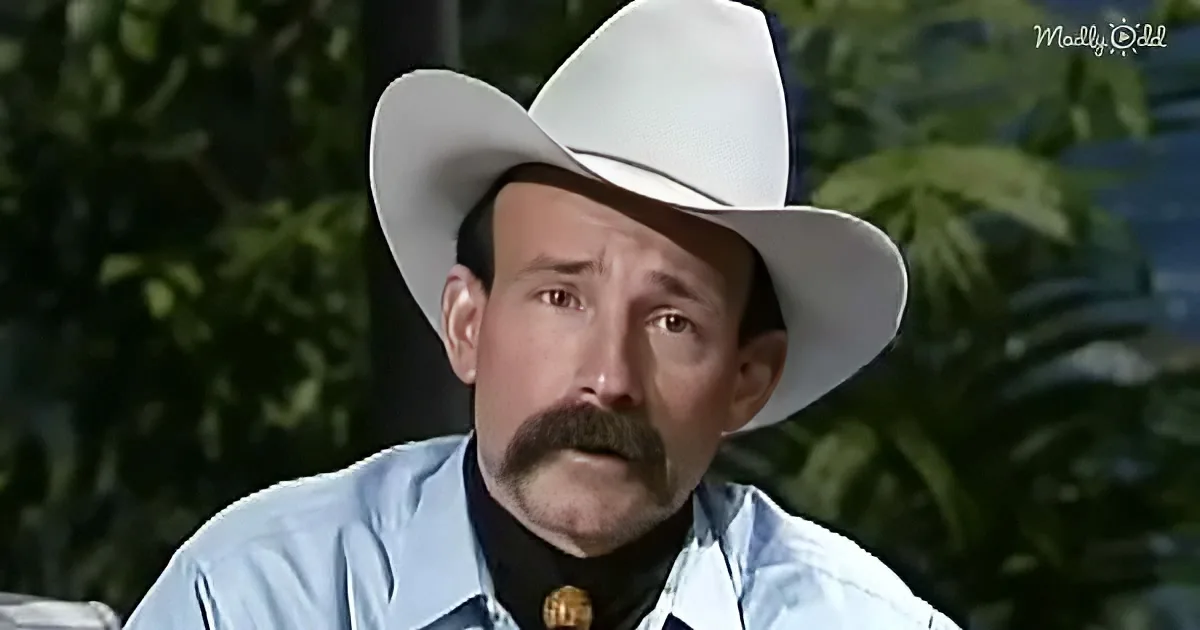A man in a white cowboy hat and blue shirt with a mustache looks concerned.