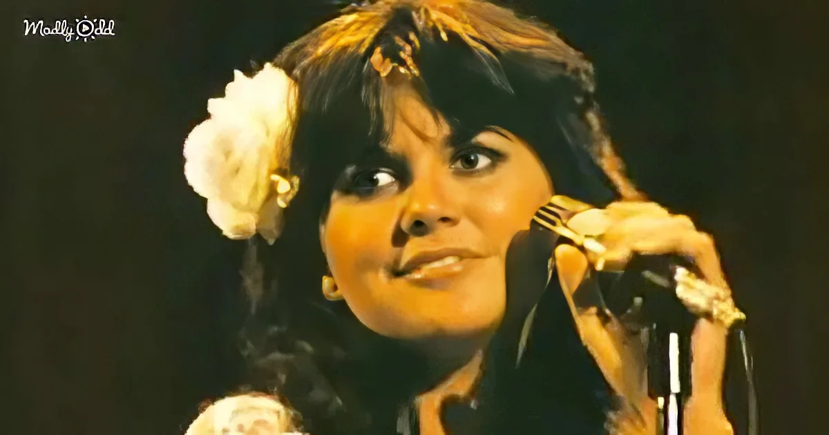 A woman with dark hair and a flower in her hair is singing into a microphone.