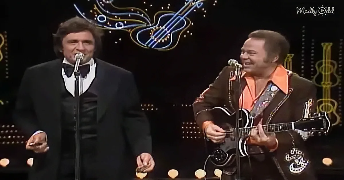 Two men on stage, one singing into a microphone, the other playing a guitar, both smiling.