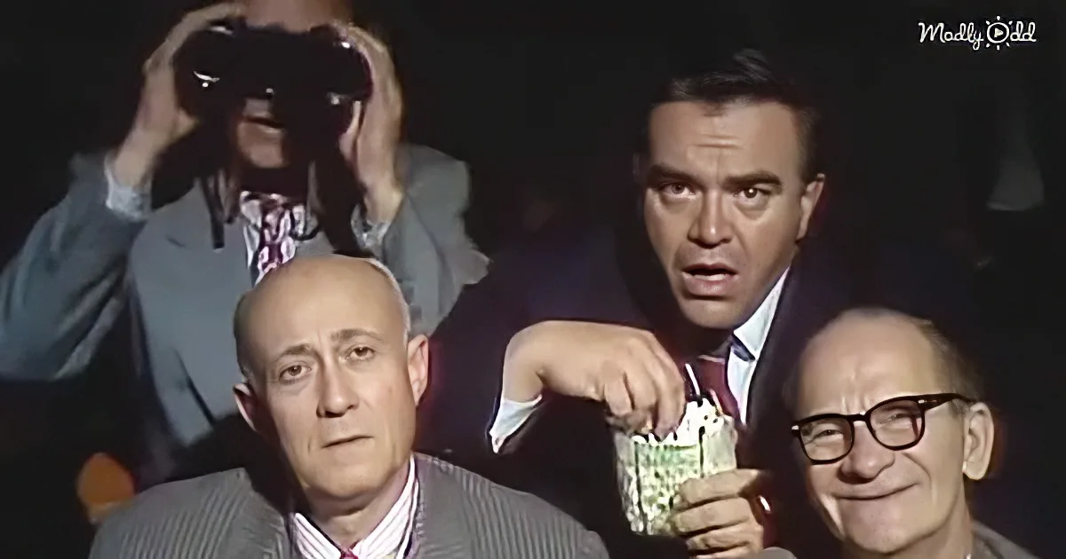 A man in a suit holds popcorn, surrounded by others in suits, one with binoculars.