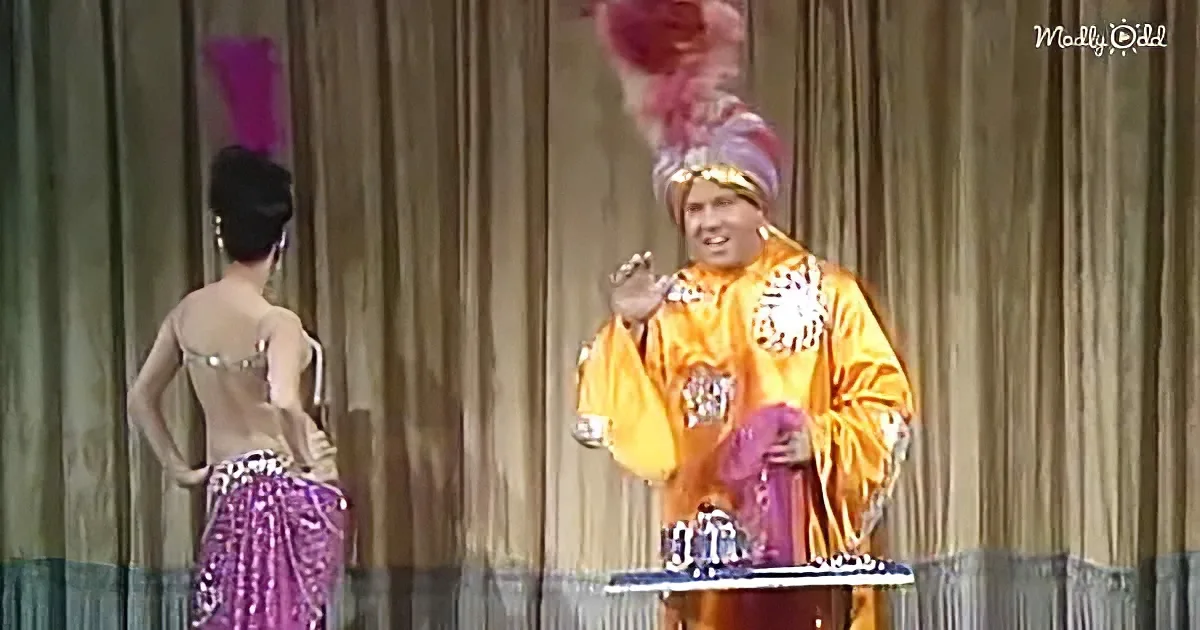 A man in a vibrant yellow costume with a purple feathered hat stands on stage, gesturing animatedly.