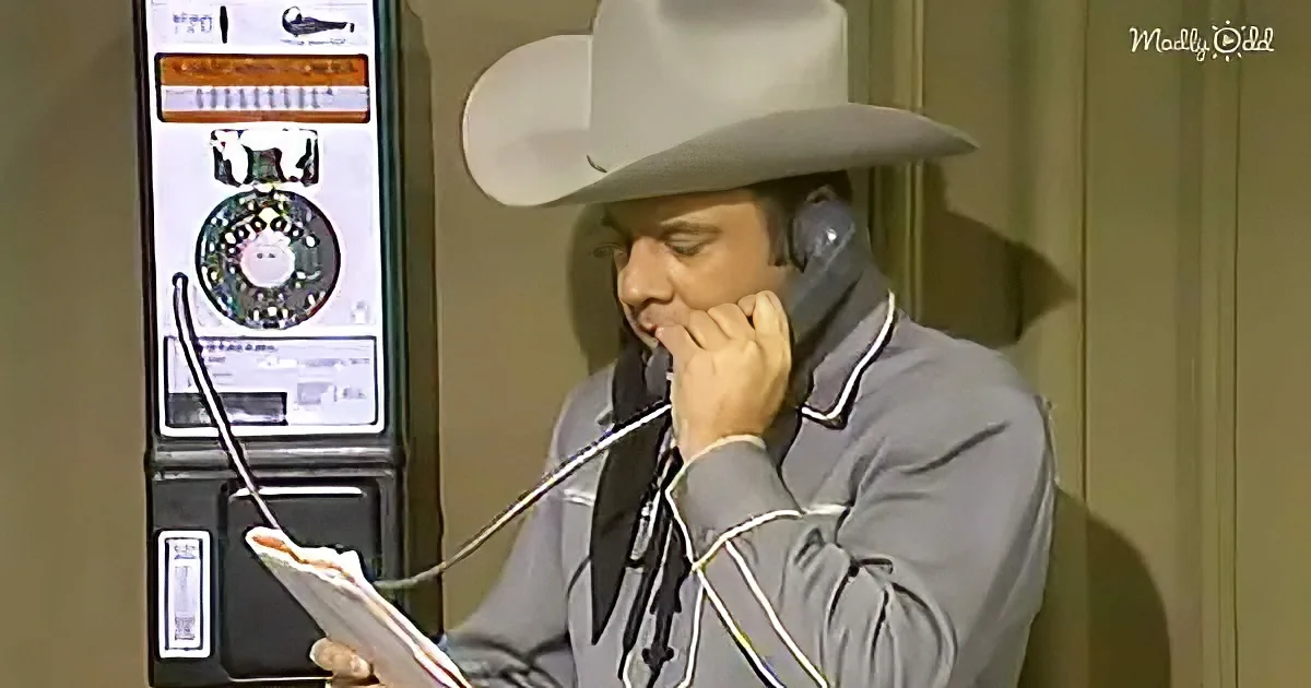 A man in a cowboy hat and gray suit talks on a rotary phone while holding a piece of paper.