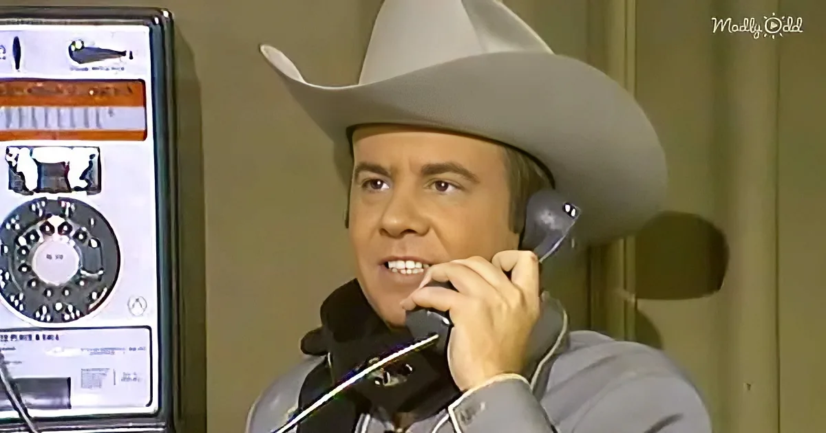 A man in a cowboy hat and white shirt is holding a phone to his ear, smiling.