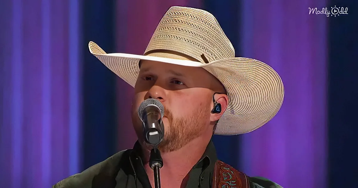 A man in a straw hat and black shirt sings into a microphone on stage.