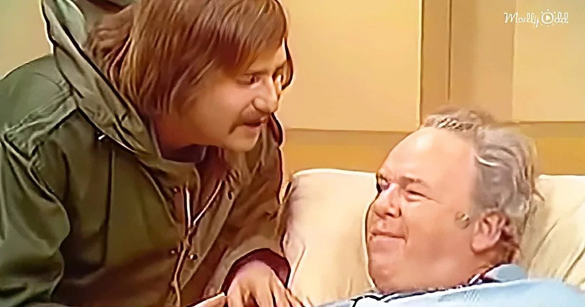 A woman in a green jacket leans over a man in a hospital bed, both smiling.