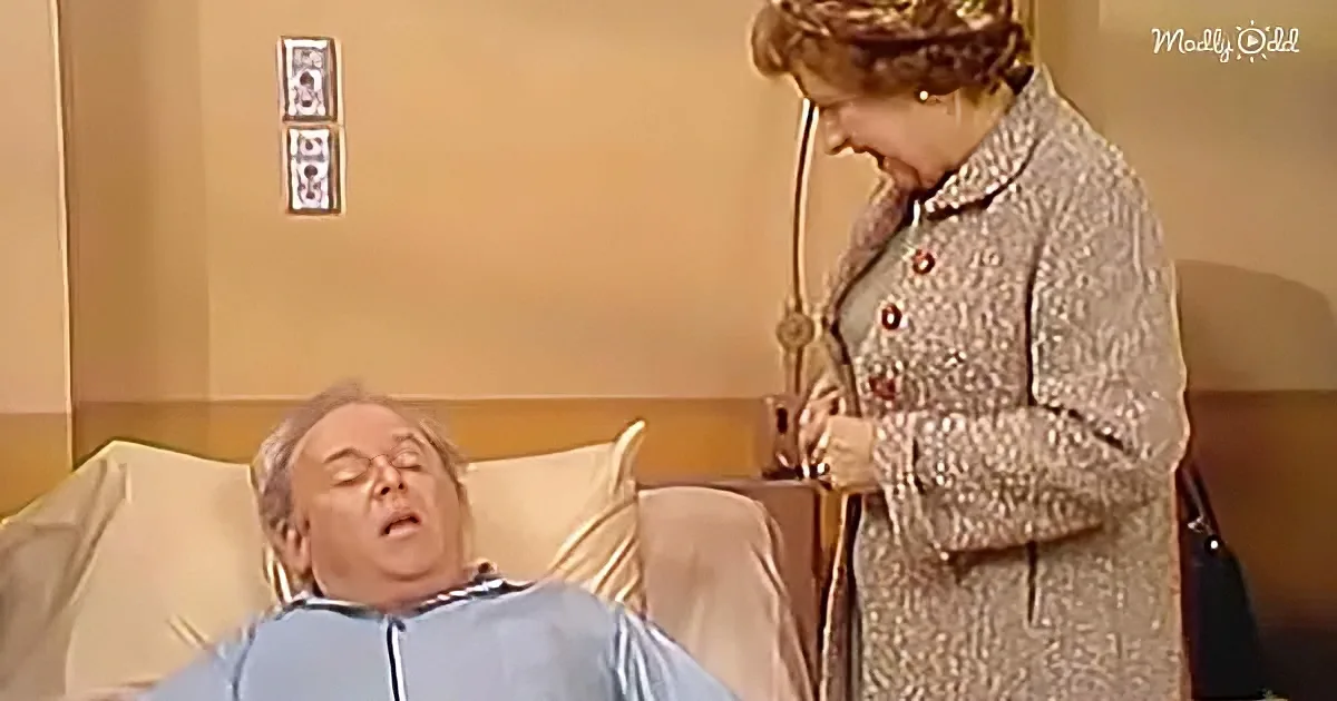 A woman in a patterned coat leans over a man in a hospital bed, holding a stethoscope.
