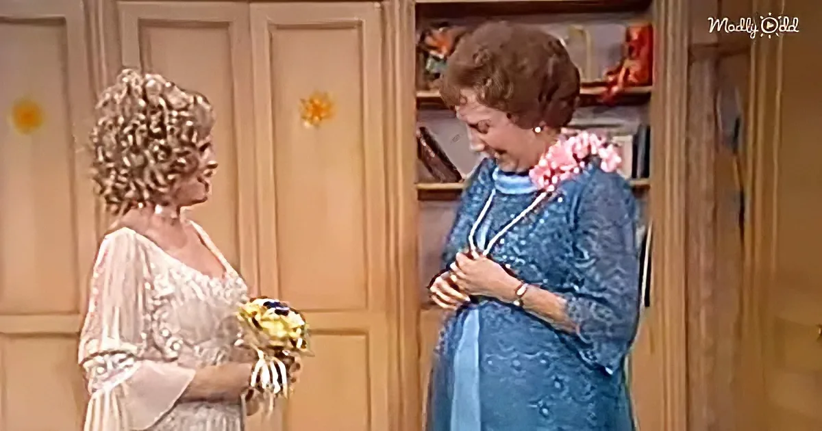 Woman in white dress holds bouquet, conversing with woman in blue dress in a room with bookshelves.