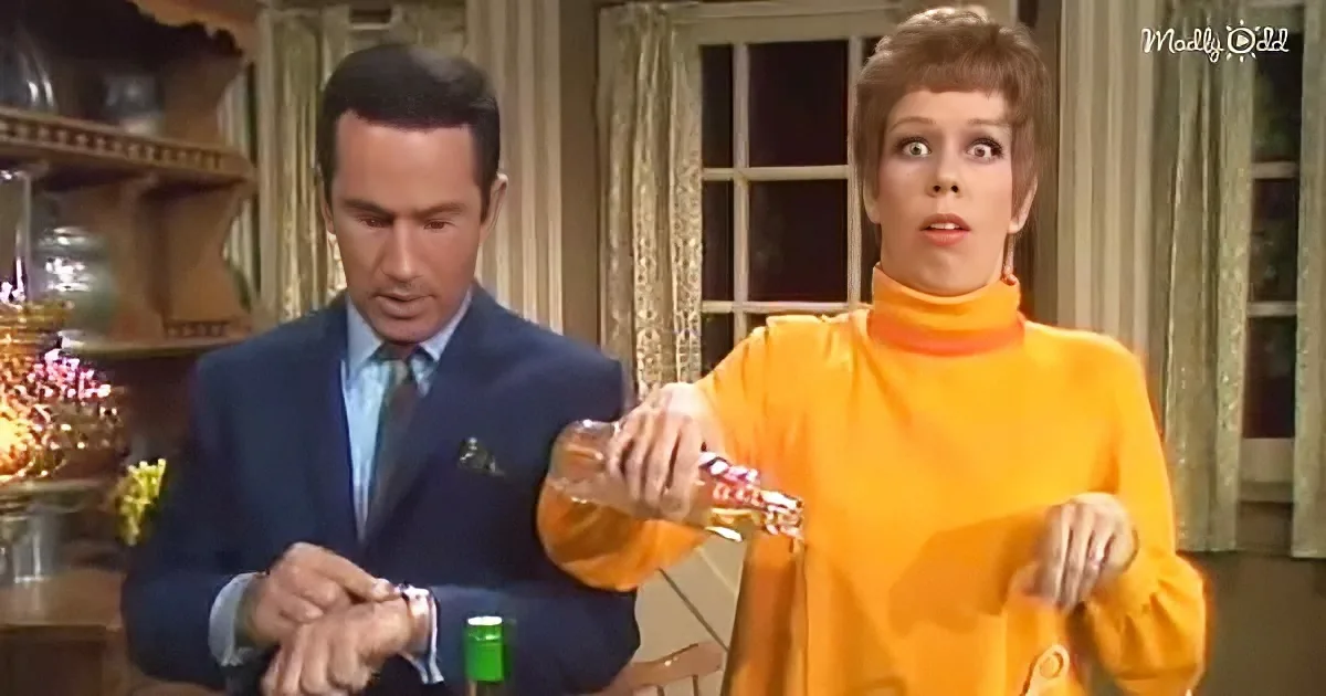 Woman in orange dress pours liquid, man in suit watches, both in a room with vintage decor.