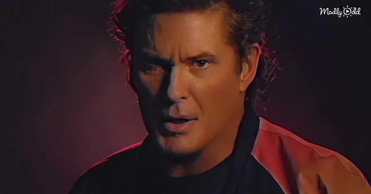 A man with dark hair and a black shirt is speaking, with a red light illuminating part of his face.