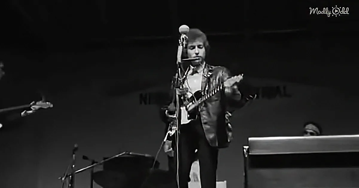 A man in a suit plays a guitar on stage, with a microphone and other instruments visible.
