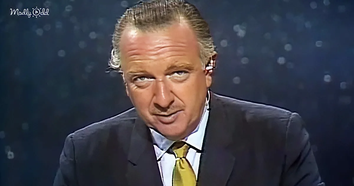 A man in a suit and yellow tie is seated, looking slightly to the side with a serious expression.