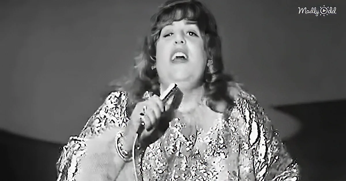 A person in a glittery outfit sings passionately into a microphone.