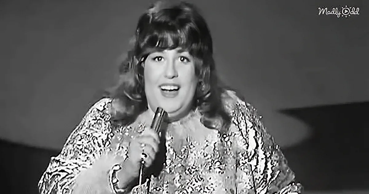 A woman in a patterned dress sings into a microphone, her hair styled in waves.