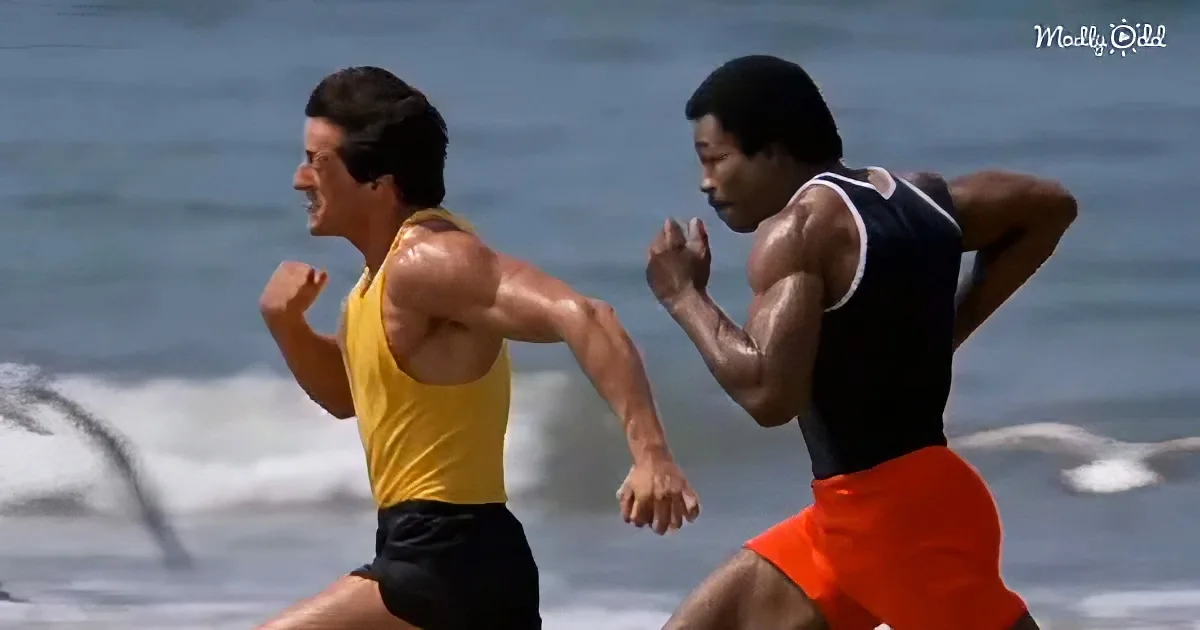 Two muscular men in athletic attire run on a beach, with waves in the background.