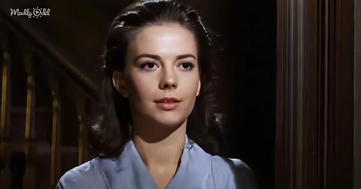 A woman in a blue uniform stands in a dimly lit room, looking slightly to the side.