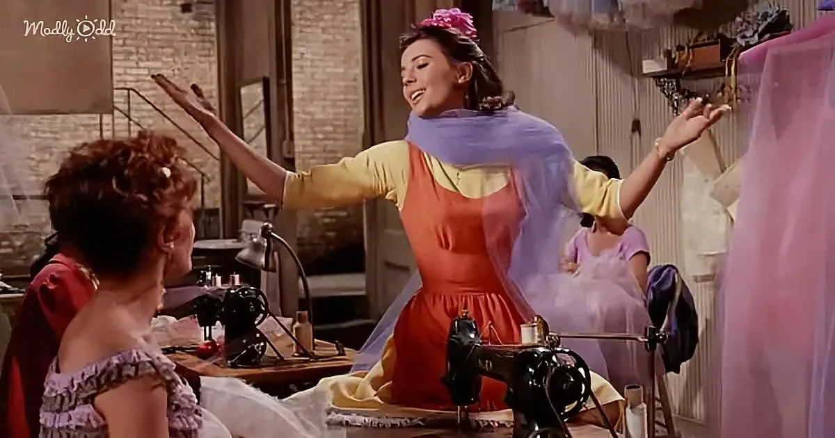A woman in a red dress and purple scarf dances joyfully in a sewing room.